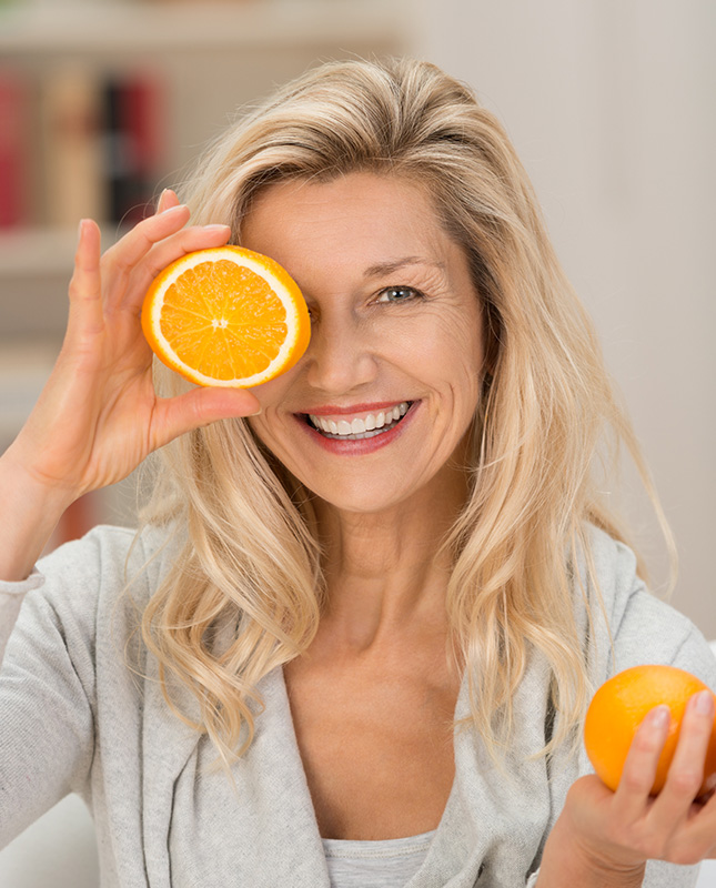 Reifere Frau hält aufgeschnittene Orange vor dem Auge und symbolisiert Smart Aging Concept - Ernährung